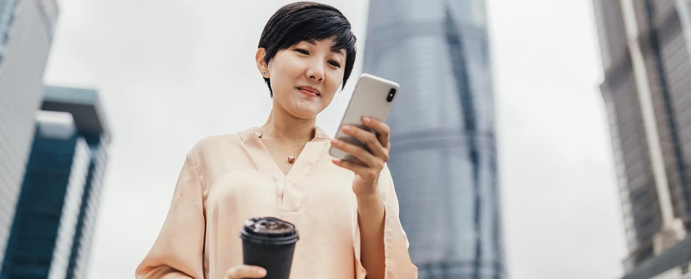 Woman holding a cup of coffee outside looking at phone